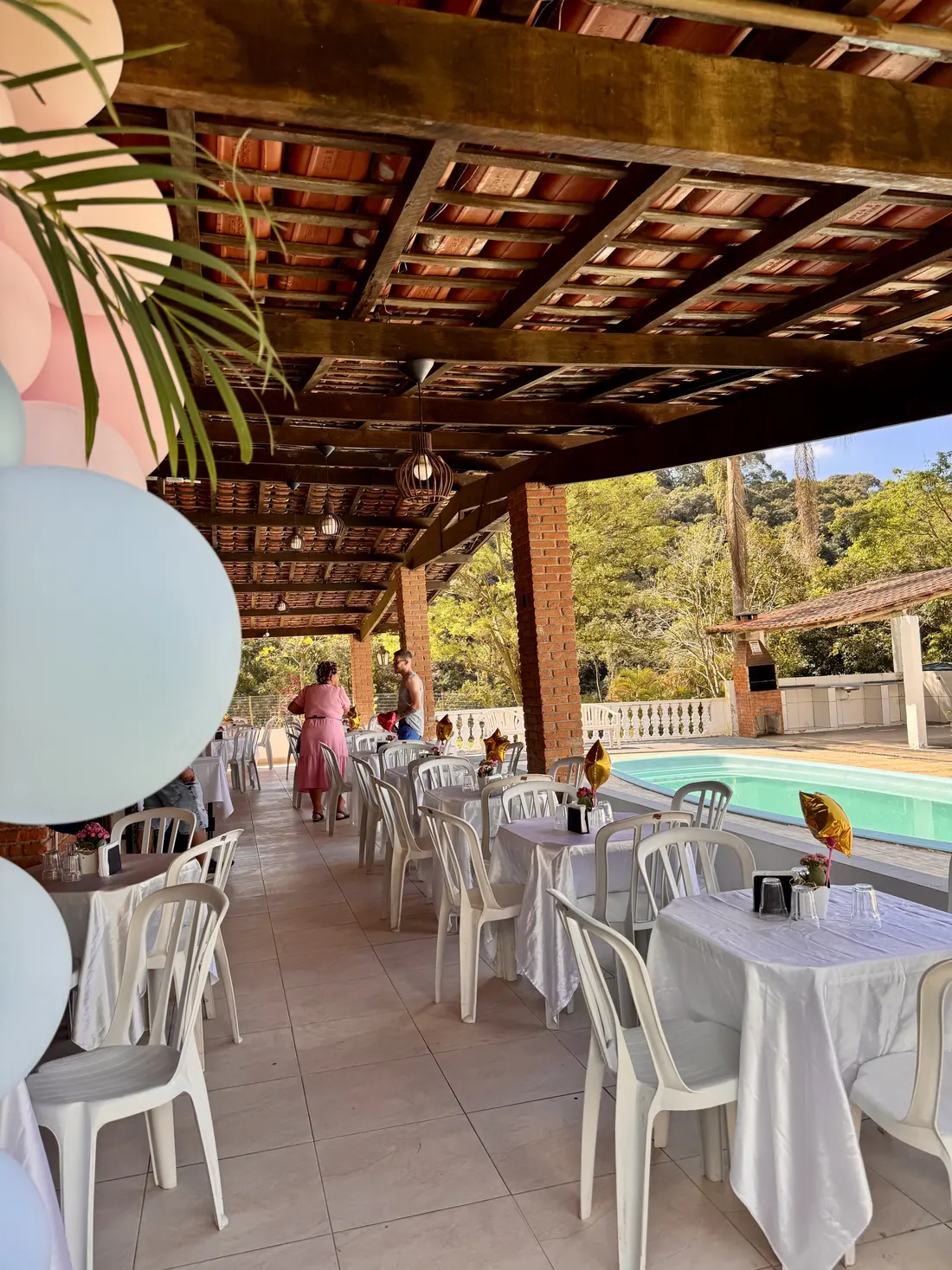 Área coberta com mesas de toalha branca, aberta para a piscina e a mata