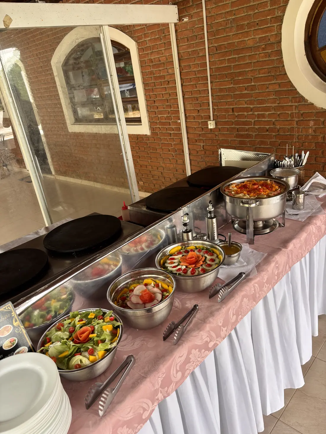 Estação de crepe com chapas, réchauds e travessas de saladas sobre toalha rosa