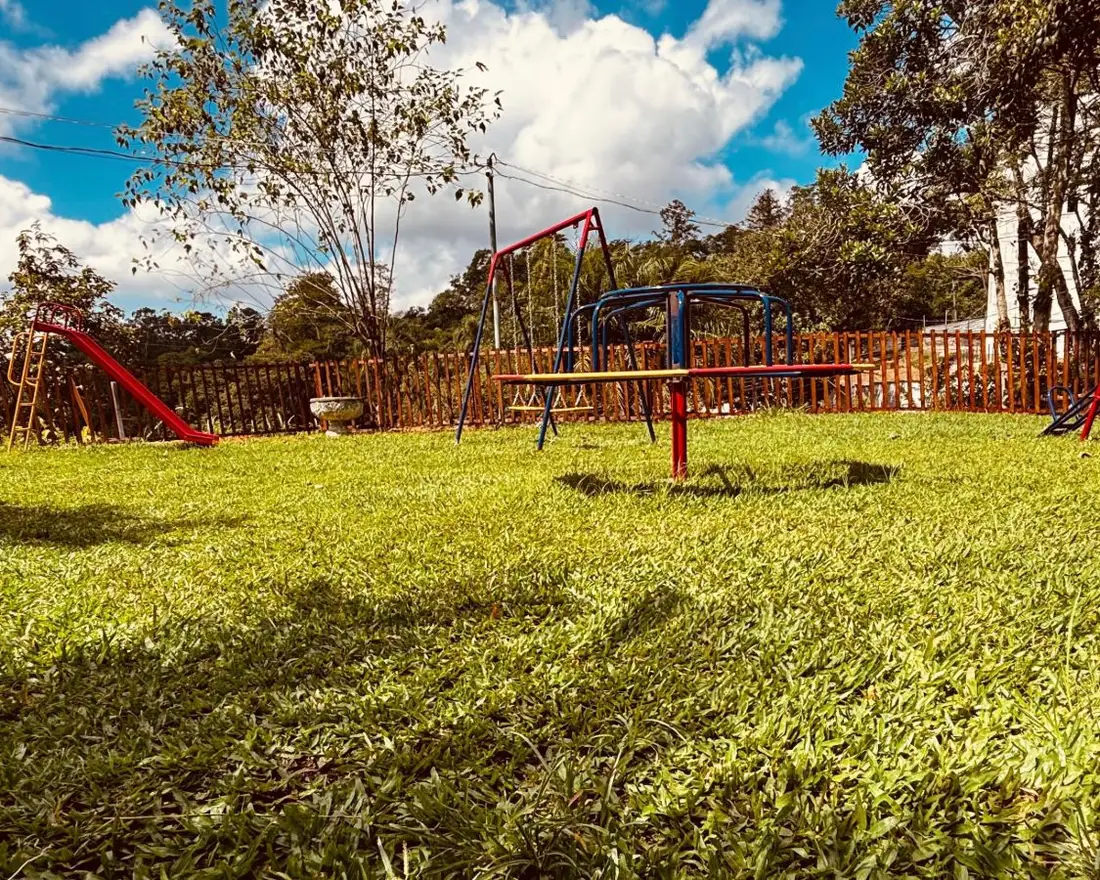 Gramado com gira-gira, balanço e escorregador, cercado por grade de madeira