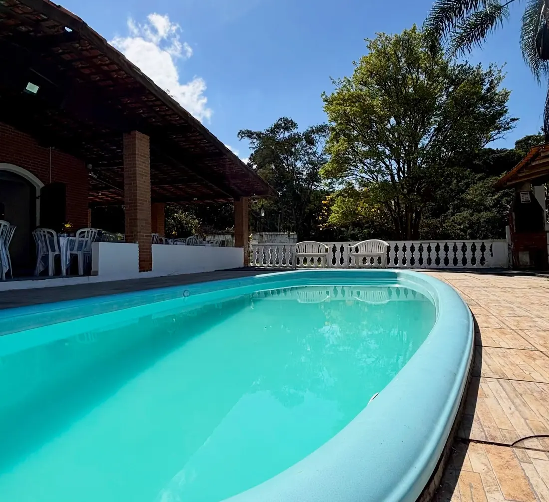 Piscina ao lado da área coberta, com mesas e jardim