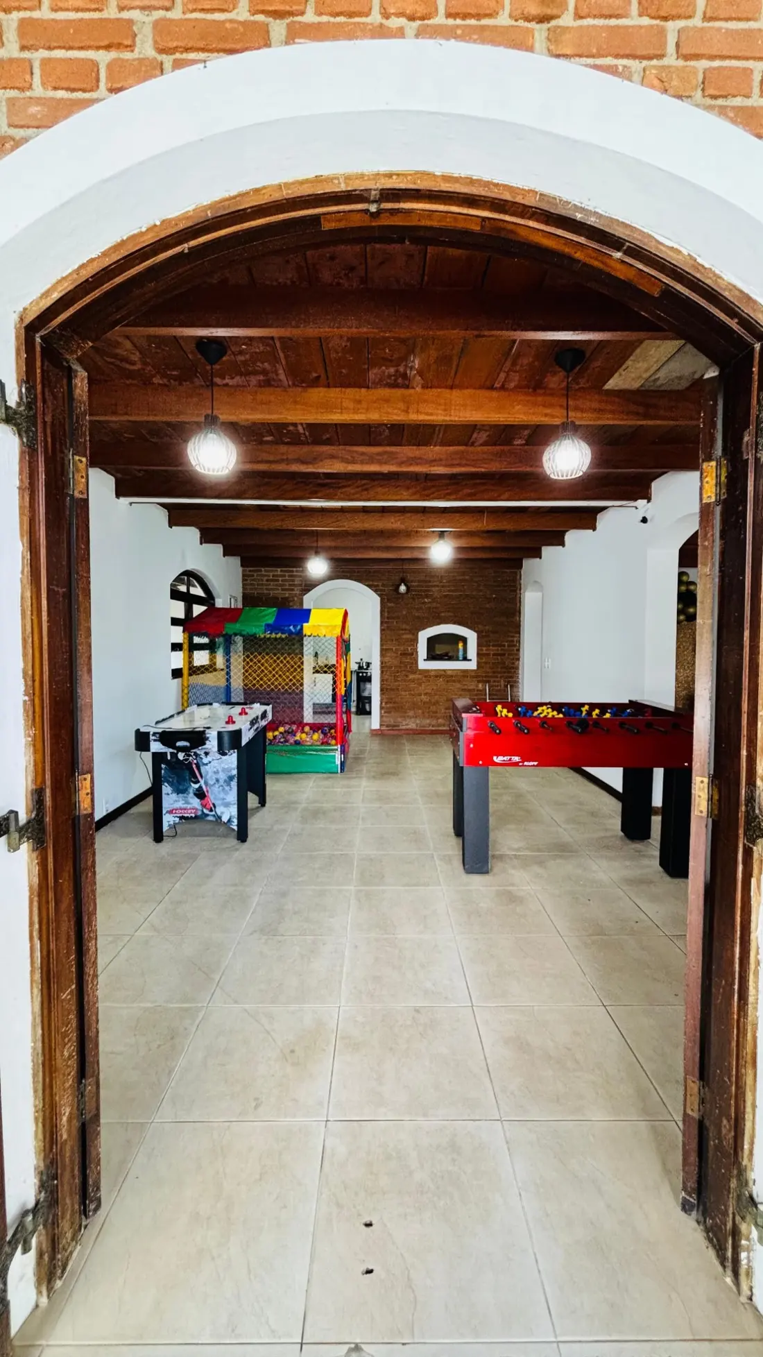 Sala de brinquedos vista pela porta em arco, com air hockey, piscina de bolinhas e pebolim