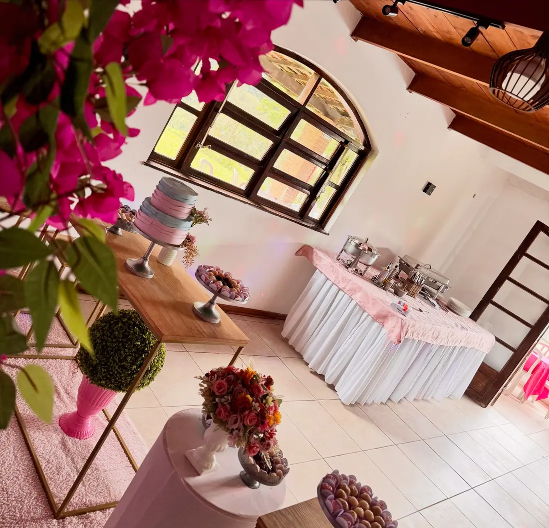 Salão com janela em arco, mesa do bolo e buffet com toalha rosa